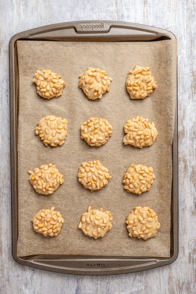 Italian Pignoli Cookies are crispy, chewy and almond-y, topped with rich, creamy pine nuts. They're sure to become a family favorite! Unbaked pignoli on a cookie sheet.