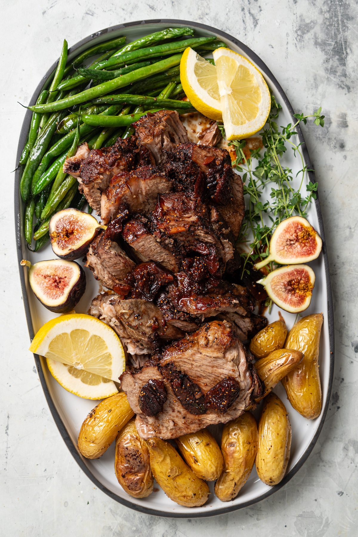 This sweet-and-savory pork shoulder recipe with honey, red wine-fig sauce, and lots of fruity figs is perfect for Thanksgiving dinners. Sliced pork shoulder recipe on a serving plate with green beans and potatoes on the side.