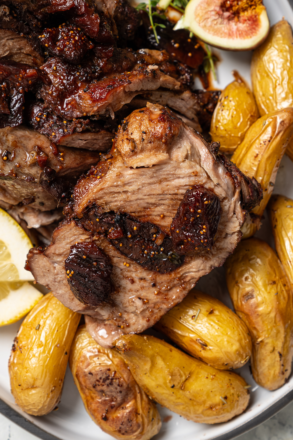 This sweet-and-savory pork shoulder recipe with honey, red wine-fig sauce, and lots of fruity figs is perfect for Thanksgiving dinners. Sliced pork shoulder recipe with fig sauce and mini potatoes on the side.