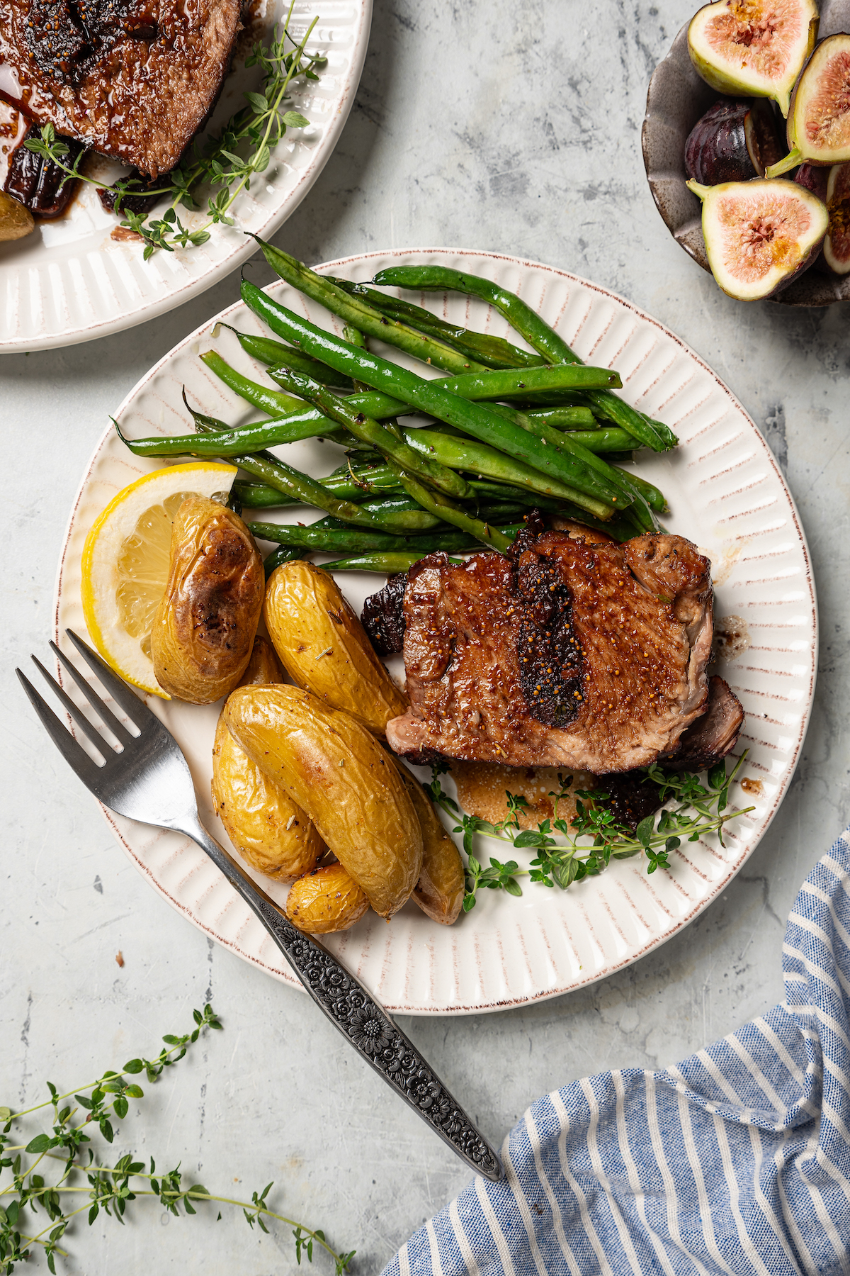 This sweet-and-savory pork shoulder recipe with honey, red wine-fig sauce, and lots of fruity figs is perfect for Thanksgiving dinners. Serving plate of roasted pork shoulder recipe with green beans and mini potatoes on the side.