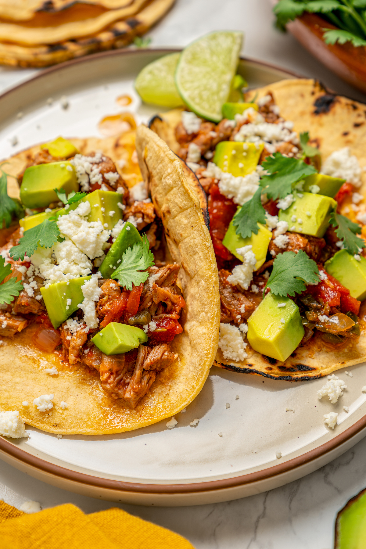 Two tacos with avocado, crumbled queso fresco, cilantro, and tomatoey pork.