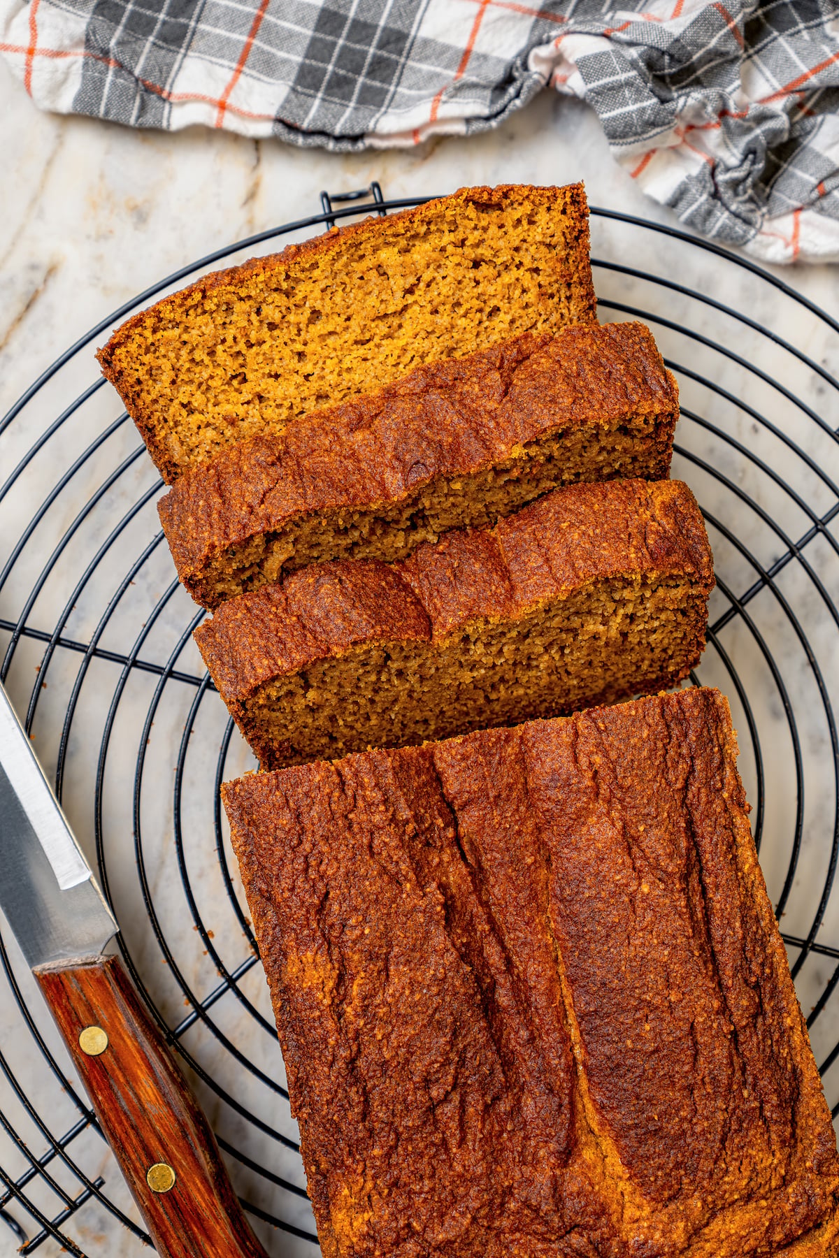 This tender paleo pumpkin bread recipe with vegan flours, coconut cream, and maple syrup is an easy fall-flavored dessert. Sliced pumpkin loaf on a cooling rack.