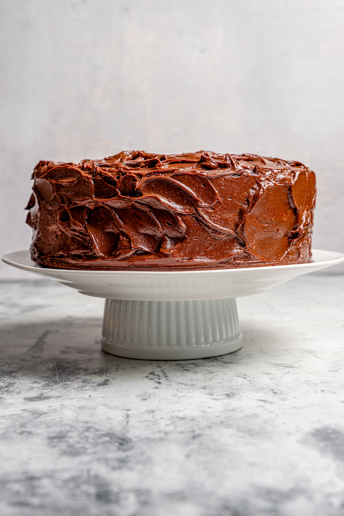 This warmly spiced pumpkin cake recipe with velvety cream cheese-chocolate frosting is a sweet end to any Thanksgiving dinner. Whole cake with chocolate frosting on a cake stand.