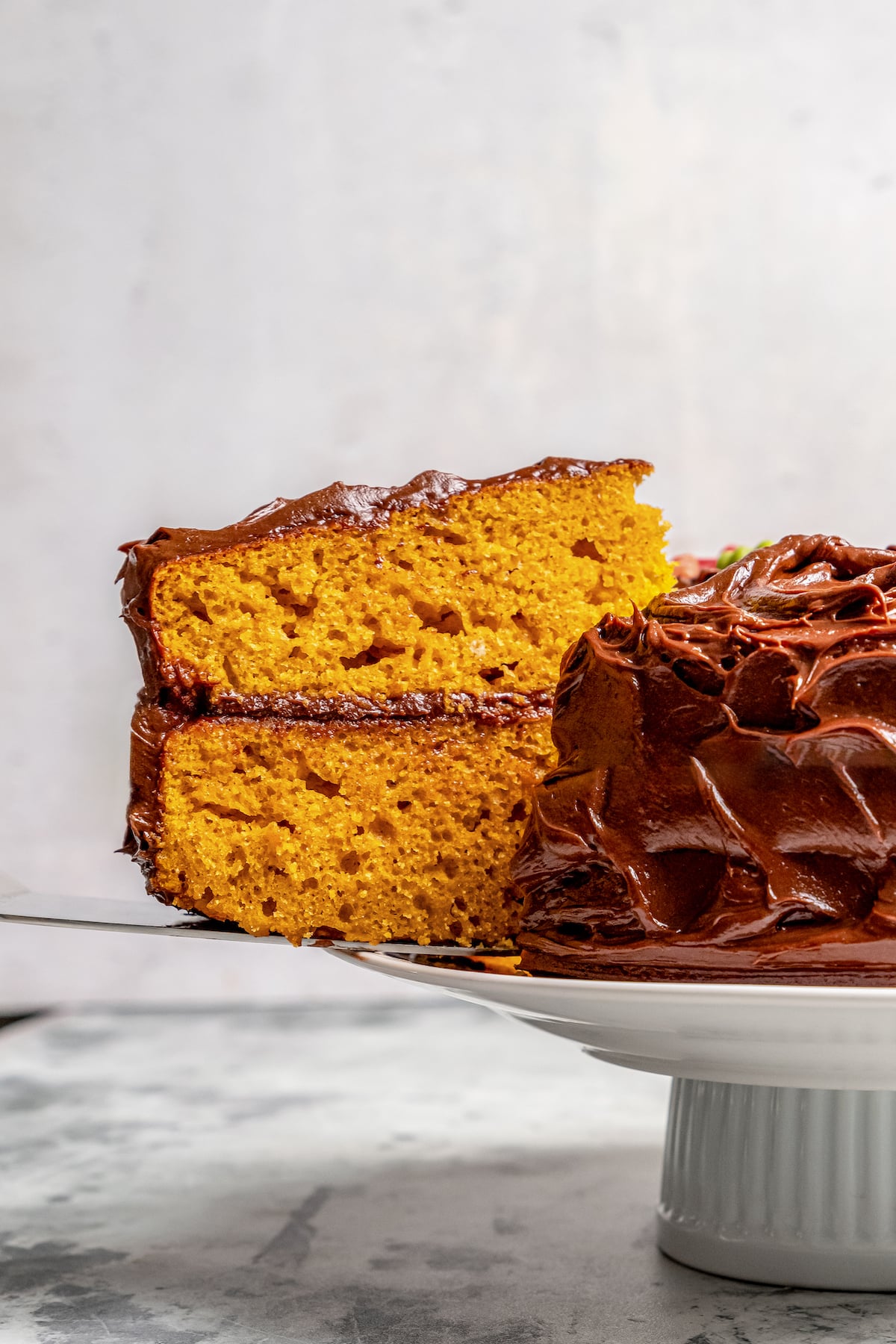 This warmly spiced pumpkin cake recipe with velvety cream cheese-chocolate frosting is a sweet end to any Thanksgiving dinner. Close-up of a tender slice of the two-layer cake with chocolate frosting.