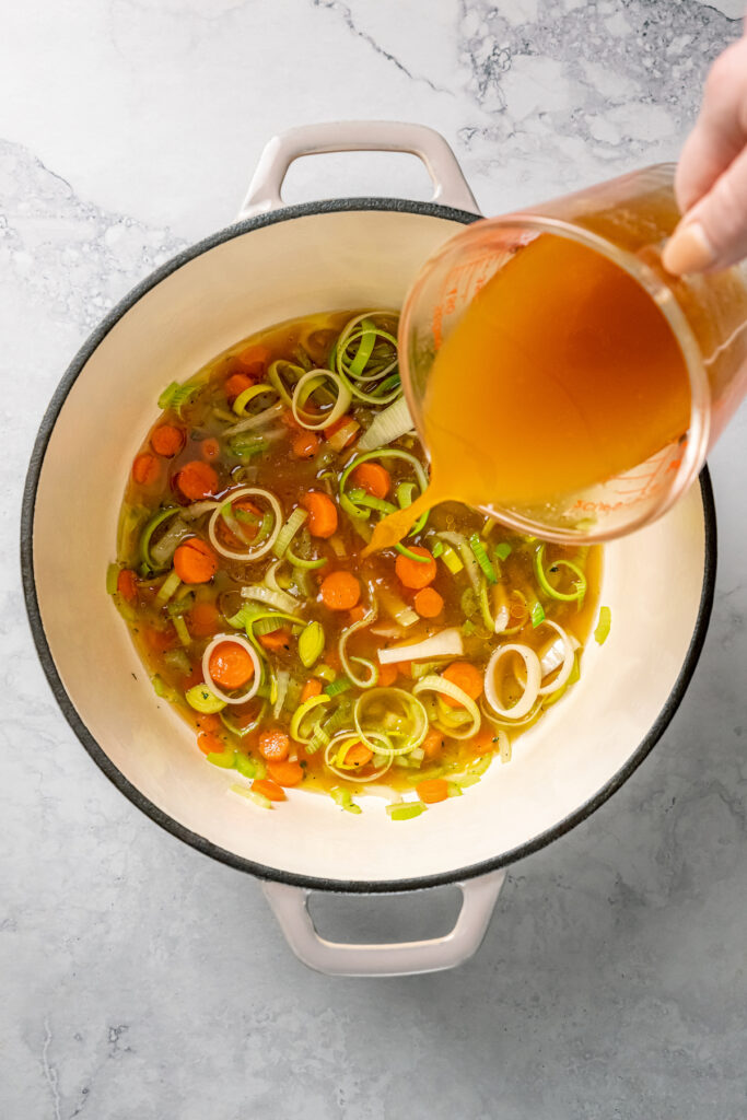 This Easy Salmon Soup is made with fresh salmon, fennel, leeks, and shitake mushrooms. It's unbelievably good, and good for your your body! Pouring vegetable broth over vegetables in a pot.