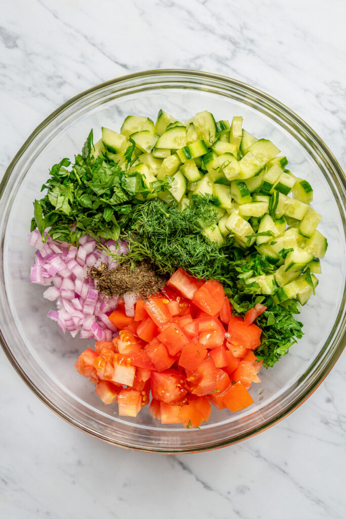 This quick shirazi salad with cucumbers, tomatoes, red onions, and a light vinaigrette is a refreshing Middle Eastern side you'll love. Cucumbers, onions, tomatoes, herbs, and mint in a bowl.