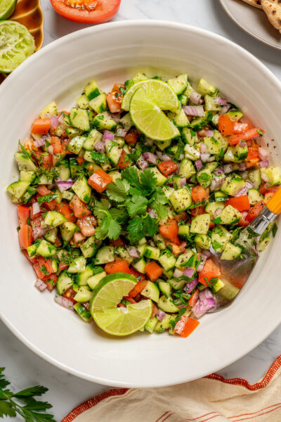 Bowl of shirazi salad with lime wedges.