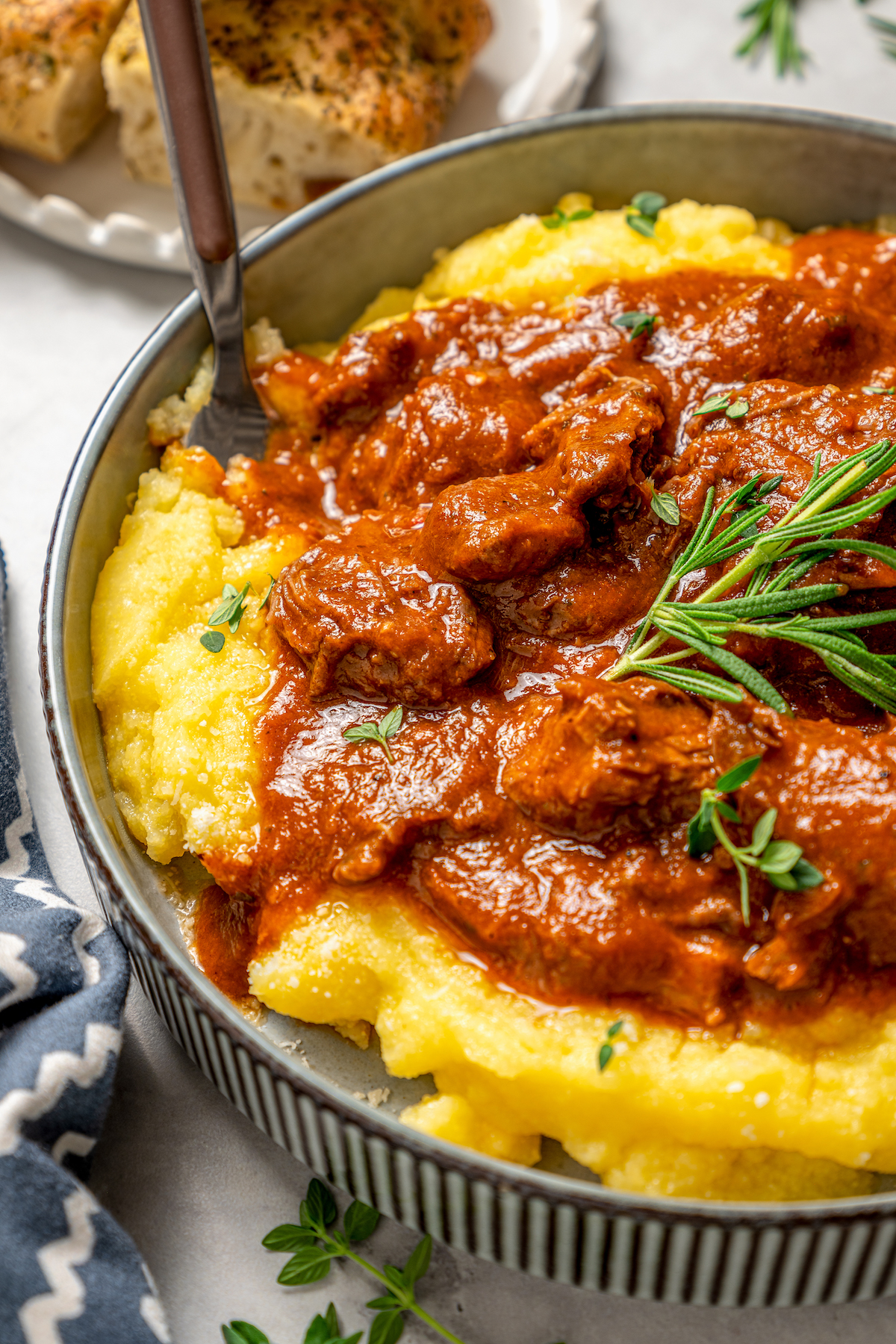 This garlicky slow cooker short ribs recipe with red wine, tender veggies, and dried herbs is an easy but fancy dinner. Angled photo of slow cooker short ribs with creamy polenta in a bowl, garnished with fresh rosemary.
