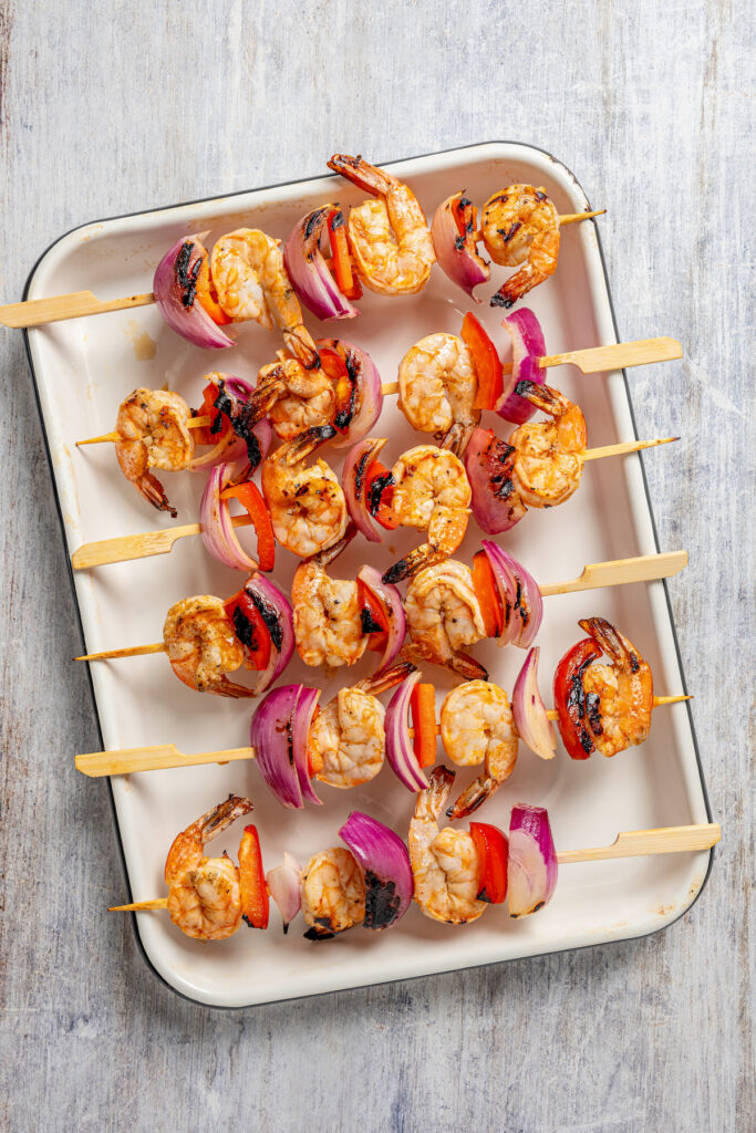 This shrimp brochette recipe with garlic-lemon marinade, sweet bell peppers, and spicy red onions is an easy 20-minute lunch. Grilled shrimp skewers on a baking sheet.