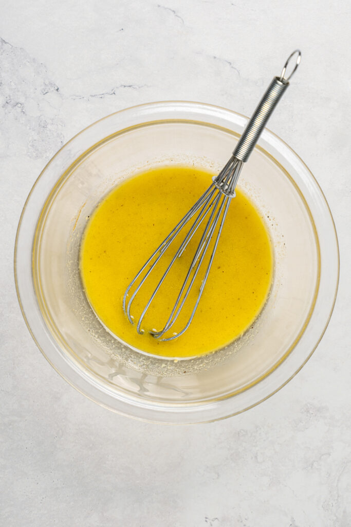 Spring Mix Salad with Champagne Dressing is elegant, flavorful, and unique - and only takes minutes to prepare! A nutritious, paleo salad. A bowl of salad dressing with a whisk resting in the dressing.