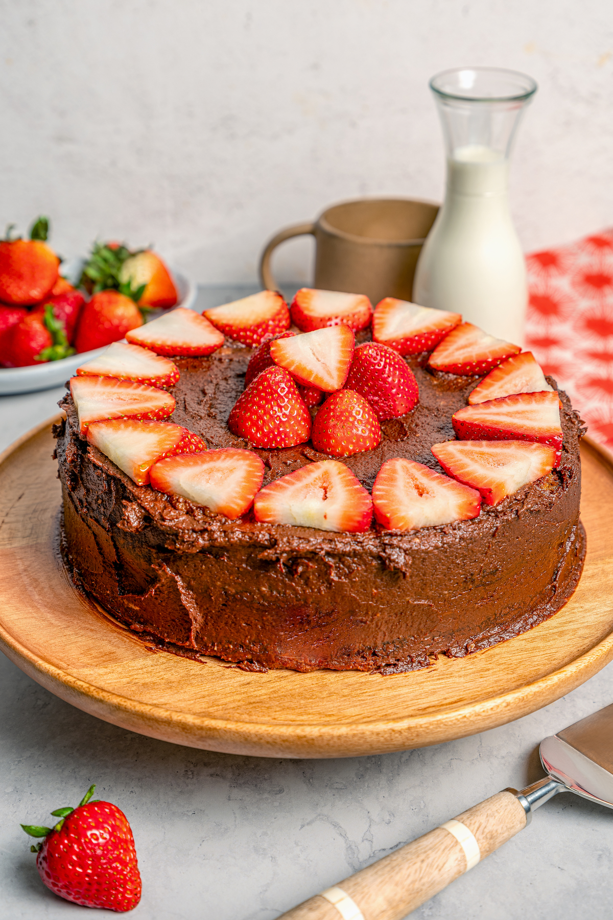 This fluffy strawberry cake recipe with homemade chocolate-maple frosting is an easy but impressive Valentine's Day dessert. Angled photo of a whole cake with chocolate frosting and sliced strawberries.