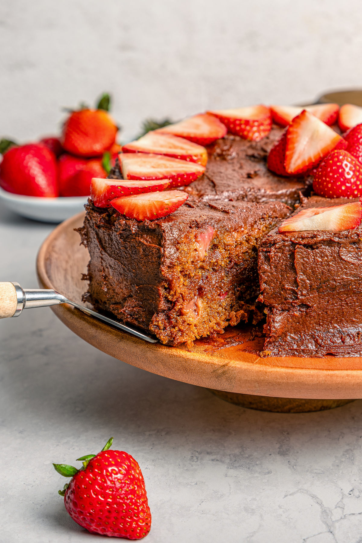 This fluffy strawberry cake recipe with homemade chocolate-maple frosting is an easy but impressive Valentine's Day dessert. Cutting into the strawberry cake with chocolate frosting.