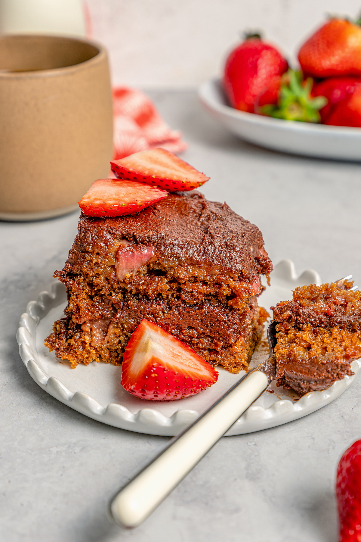 This fluffy strawberry cake recipe with homemade chocolate-maple frosting is an easy but impressive Valentine's Day dessert. Digging into a slice of cake with chocolate frosting.