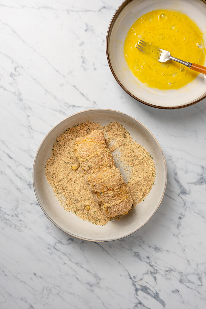 Stuffed Chicken Breasts pack so much flavor in every bite! With goat cheese, basil and white wine mushroom sauce, it's fancy but easy to make. A rolled up chicken breast, being coated in breadcrumbs.