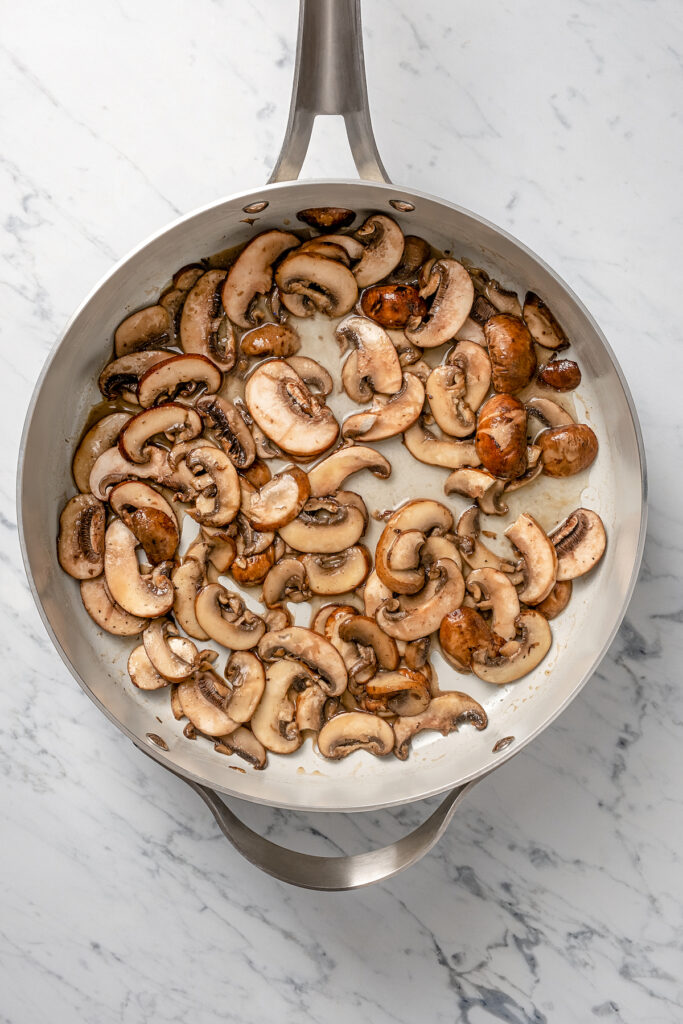 Stuffed Chicken Breasts pack so much flavor in every bite! With goat cheese, basil and white wine mushroom sauce, it's fancy but easy to make. Sauteed mushrooms in a pan.