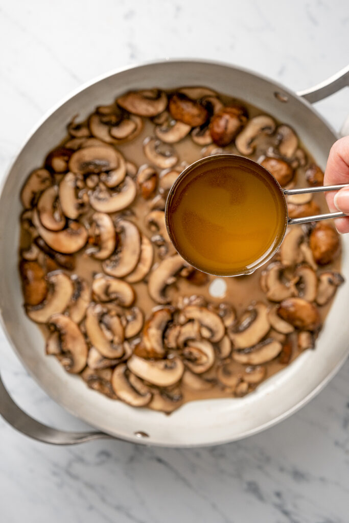 Stuffed Chicken Breasts pack so much flavor in every bite! With goat cheese, basil and white wine mushroom sauce, it's fancy but easy to make. Chicken broth being poured into a pan of sauteed mushrooms.