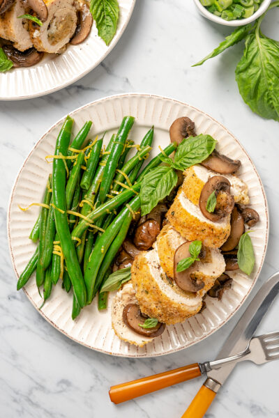 A dinner plate with a sliced stuffed chicken breast and lemony green beans.