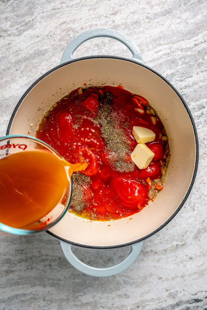 This easy tomato bisque recipe with parmesan and Italian seasoning is a comforting weeknight dinner paired with toasty sliced bread. Pouring the broth into the pot with butter, tomatoes, sauteed veggies, and wine.