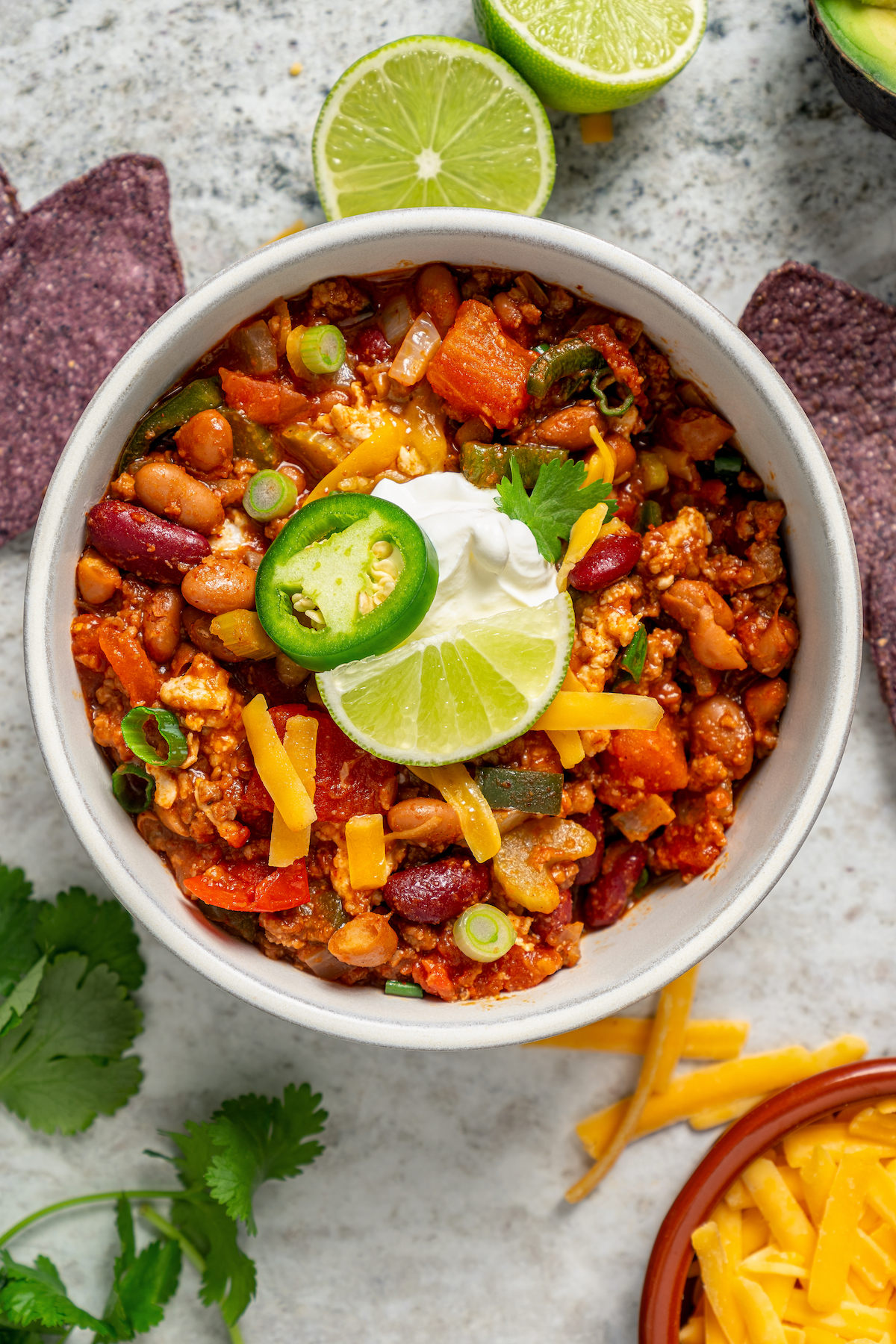 This freezer-friendly turkey chili recipe with beans, bell peppers, onions, and tomatoes is a smokey and spicy Tex-Mex weeknight dinner. Bowl of turkey chili with a dollop of sour cream, fresh jalapeño, and a lime wedge on top.