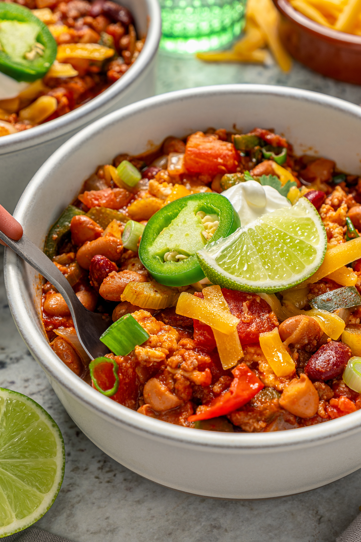 This freezer-friendly turkey chili recipe with beans, bell peppers, onions, and tomatoes is a smokey and spicy Tex-Mex weeknight dinner. Angled photo of freshly made chili with sour cream, a jalapeño slice, and a lime wedge on top.