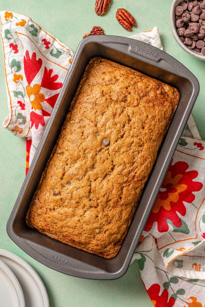 This tender zucchini bread recipe with cinnamon, earthy nutmeg, and semi-sweet chocolate chips is an easy way to sneak veggies into dessert. Baked zucchini loaf with golden edges.