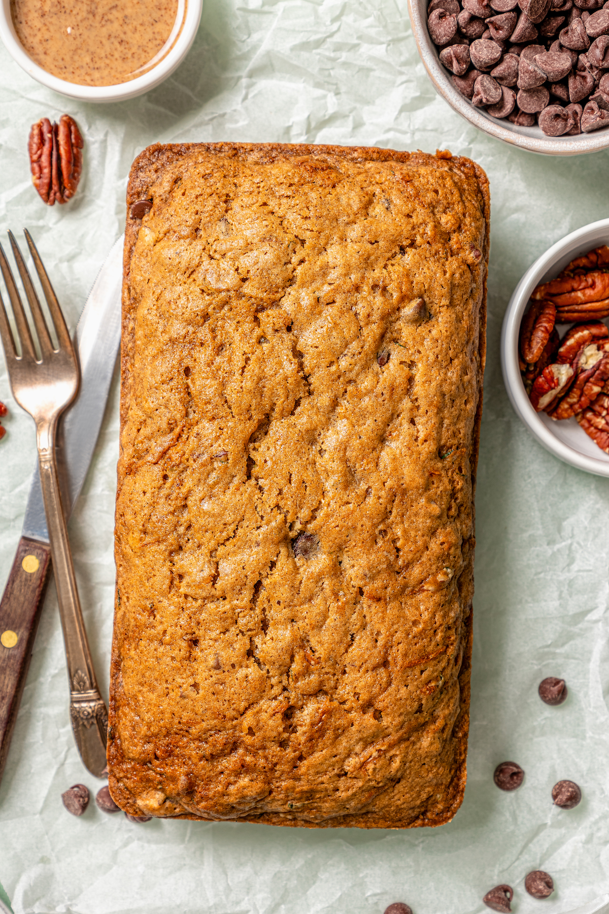 This tender zucchini bread recipe with cinnamon, earthy nutmeg, and semi-sweet chocolate chips is an easy way to sneak veggies into dessert. Golden, freshly-baked loaf.