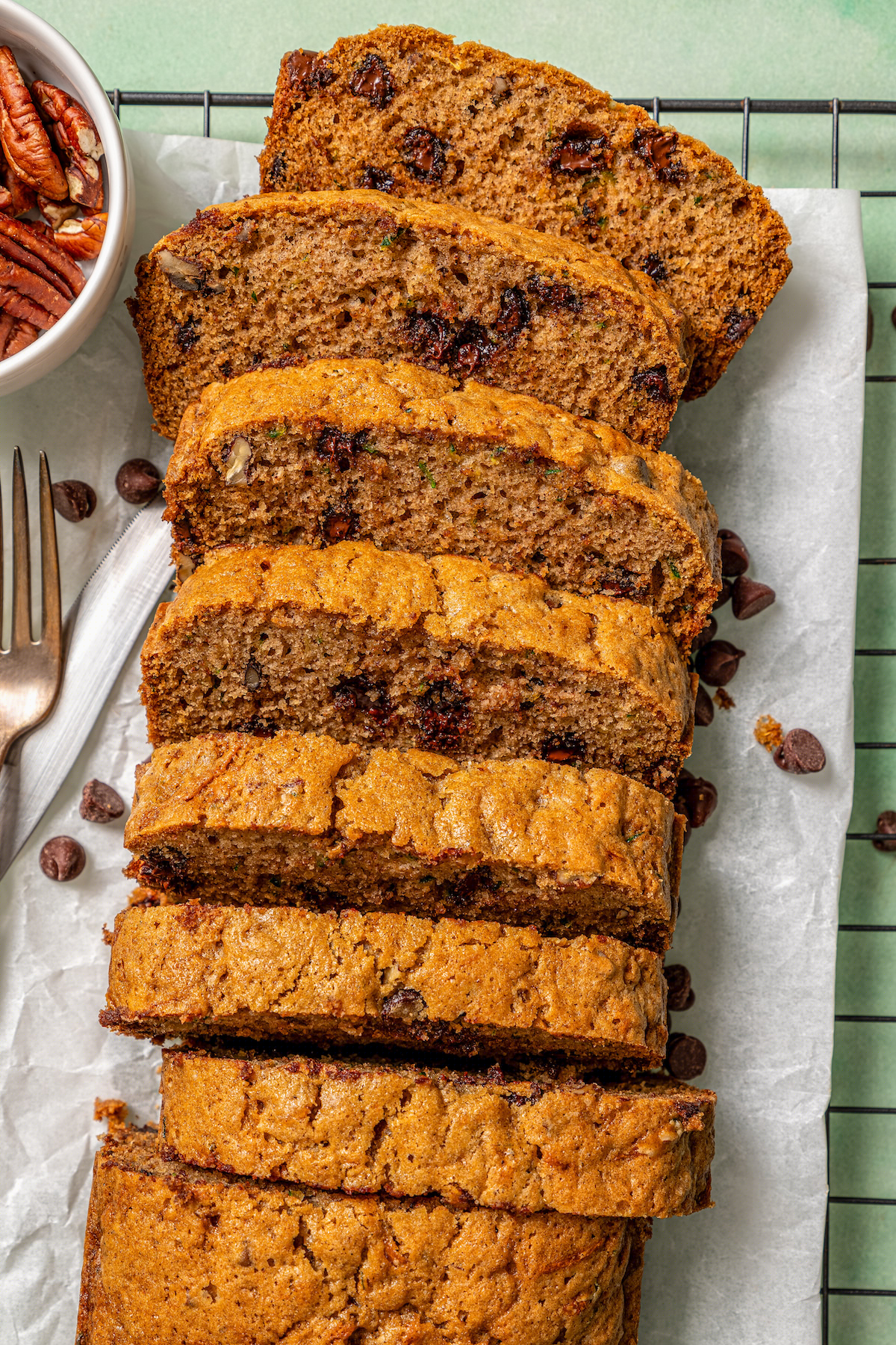 This tender zucchini bread recipe with cinnamon, earthy nutmeg, and semi-sweet chocolate chips is an easy way to sneak veggies into dessert. Sliced loaf with fresh zucchini and chocolate chips inside.